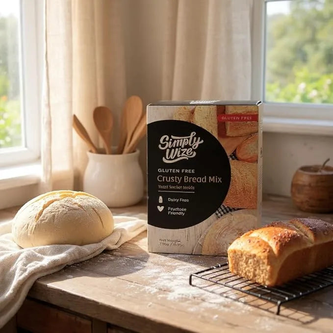 Box of Simply Wize gluten-free crusty bread mix on a wooden table with baked bread and utensils.
